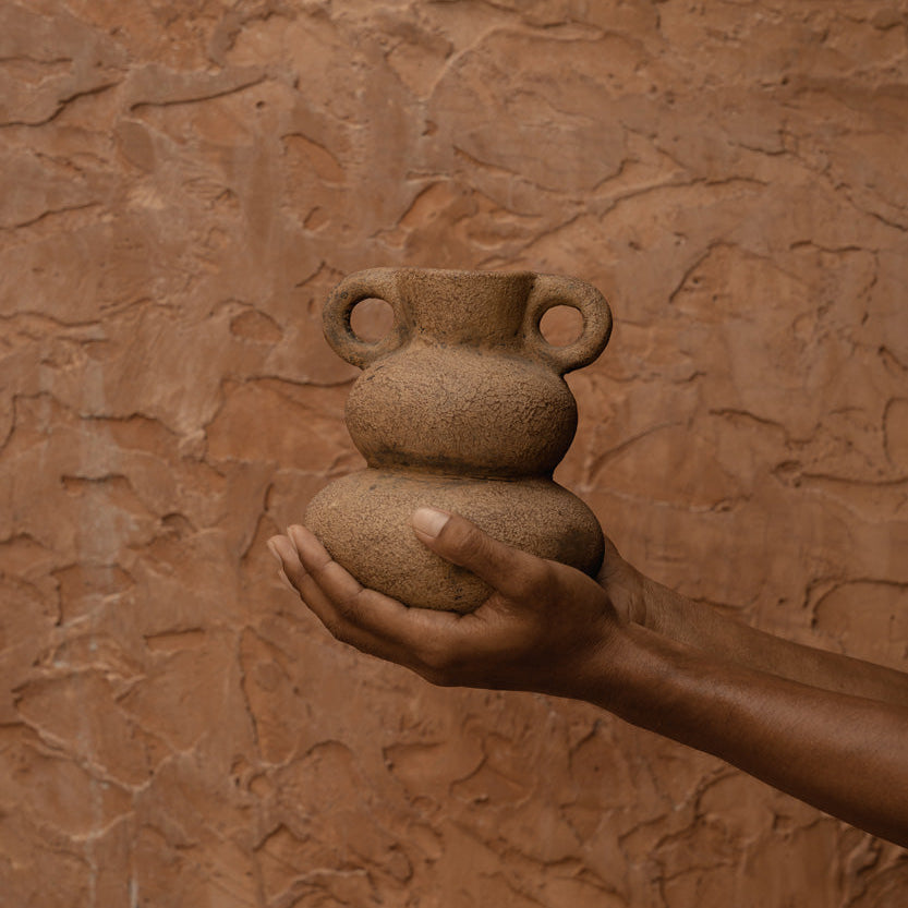 Hand holding a terracotta vase against a textured brown wall