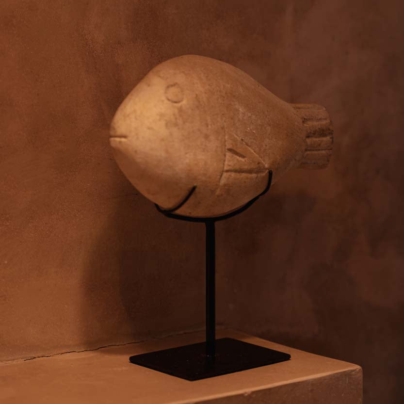 Stone fish sculpture on a stand against a brown textured wall