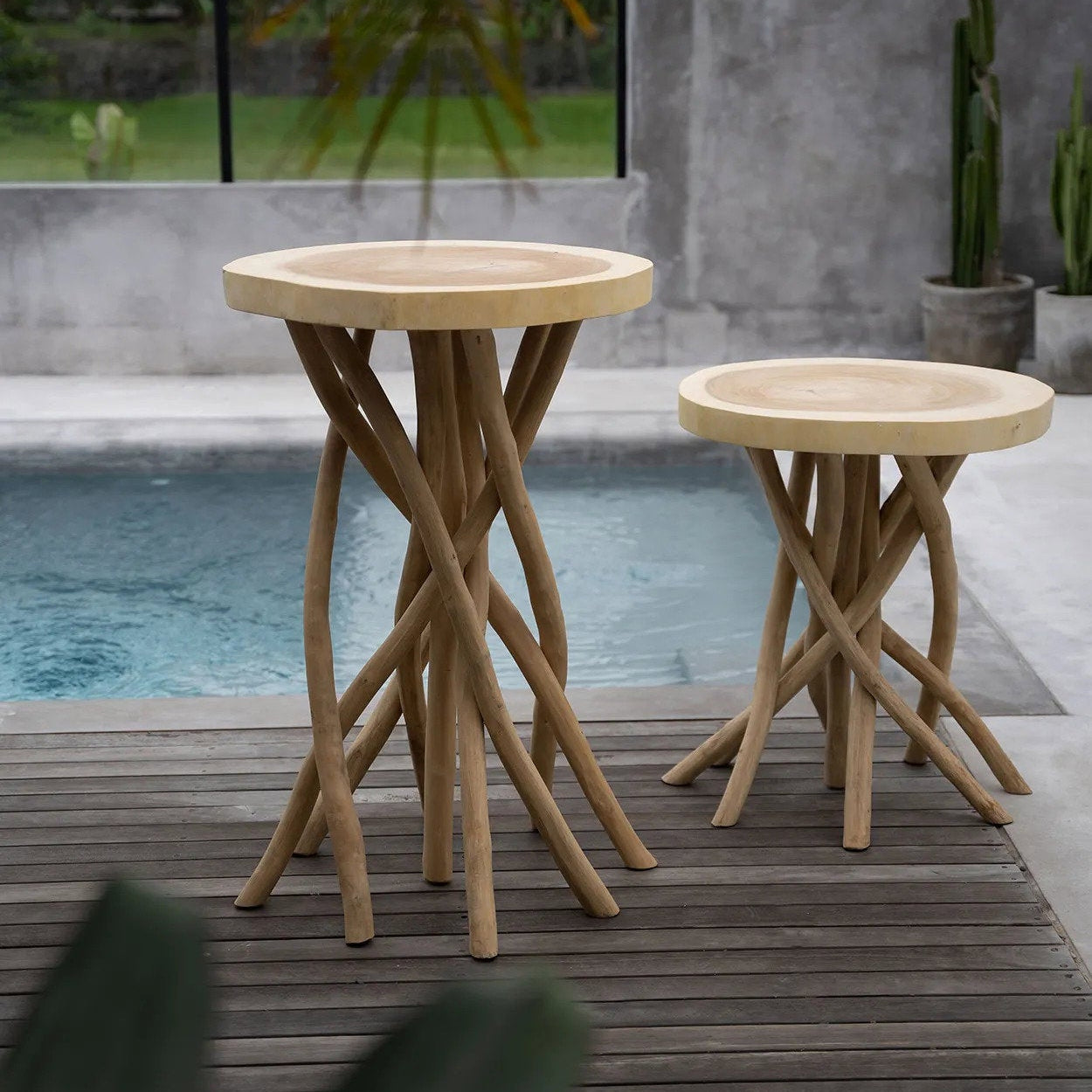 Two wooden side tables on a wooden deck by a poolside with a blurred background