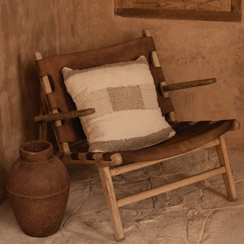 Wooden chair with a cushion and a terracotta vase against a textured wall.
