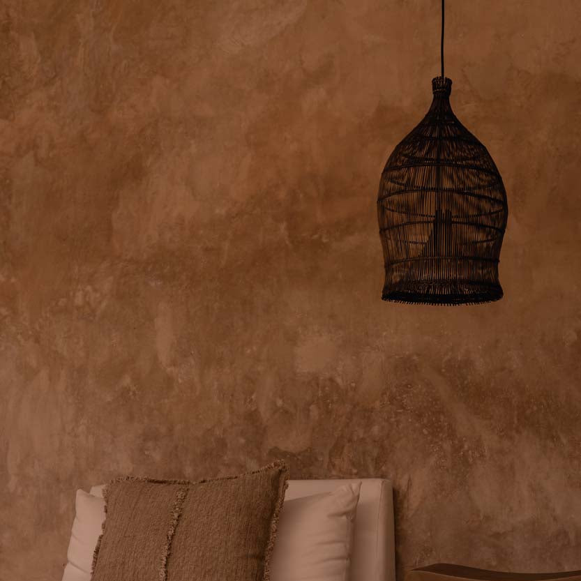 Woven bamboo pendant light hanging against a textured wall in an interior with  bed.