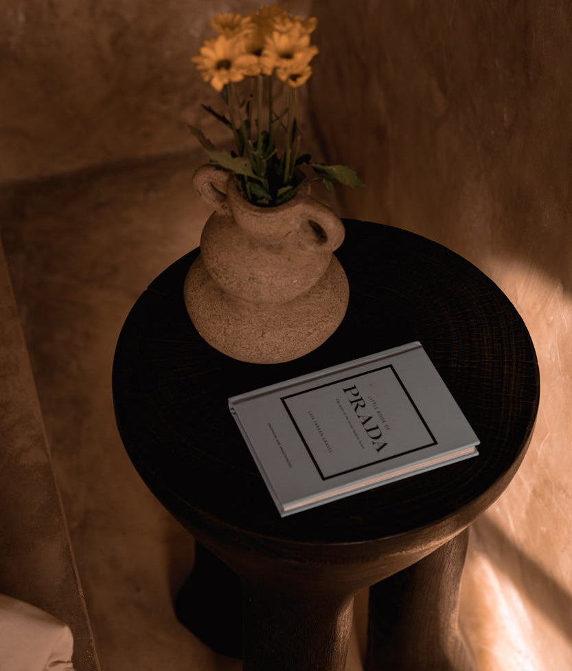 Small round wooden side table with a vase of flowers and a book on a soft, warm-toned background