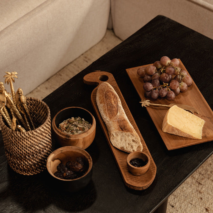 Wooden cutting board with bread and grapes on a dark wooden coffee table.