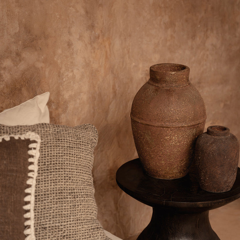Decorative setting with textured pillows and rustic vases against a beige wall.