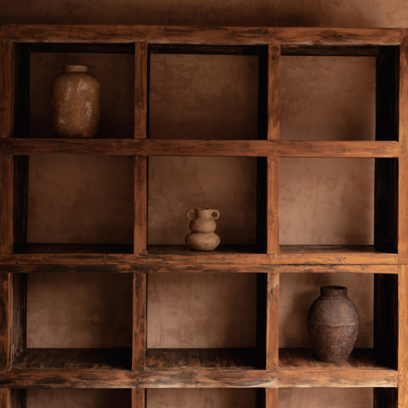 Wooden shelf with terracotta vases against a brown wall