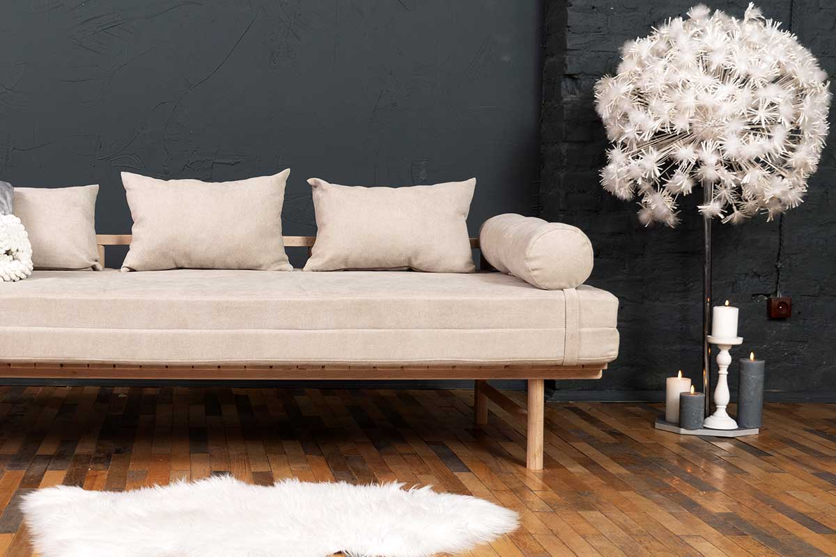 A wooden daybed with a beige mattress and cushions that can easily be transformed into a double bed