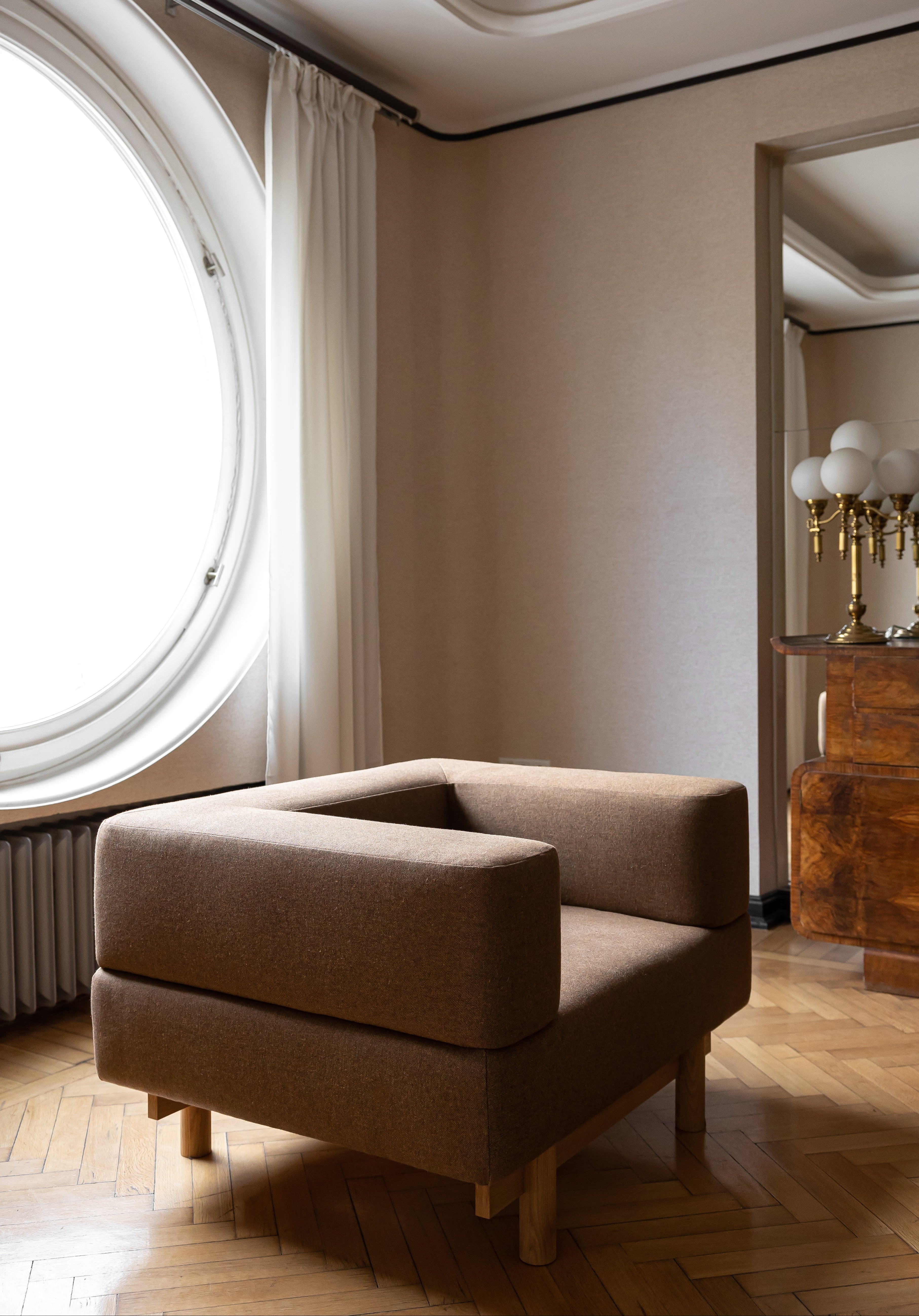Brown armchair in a room with a round window and wooden floor.